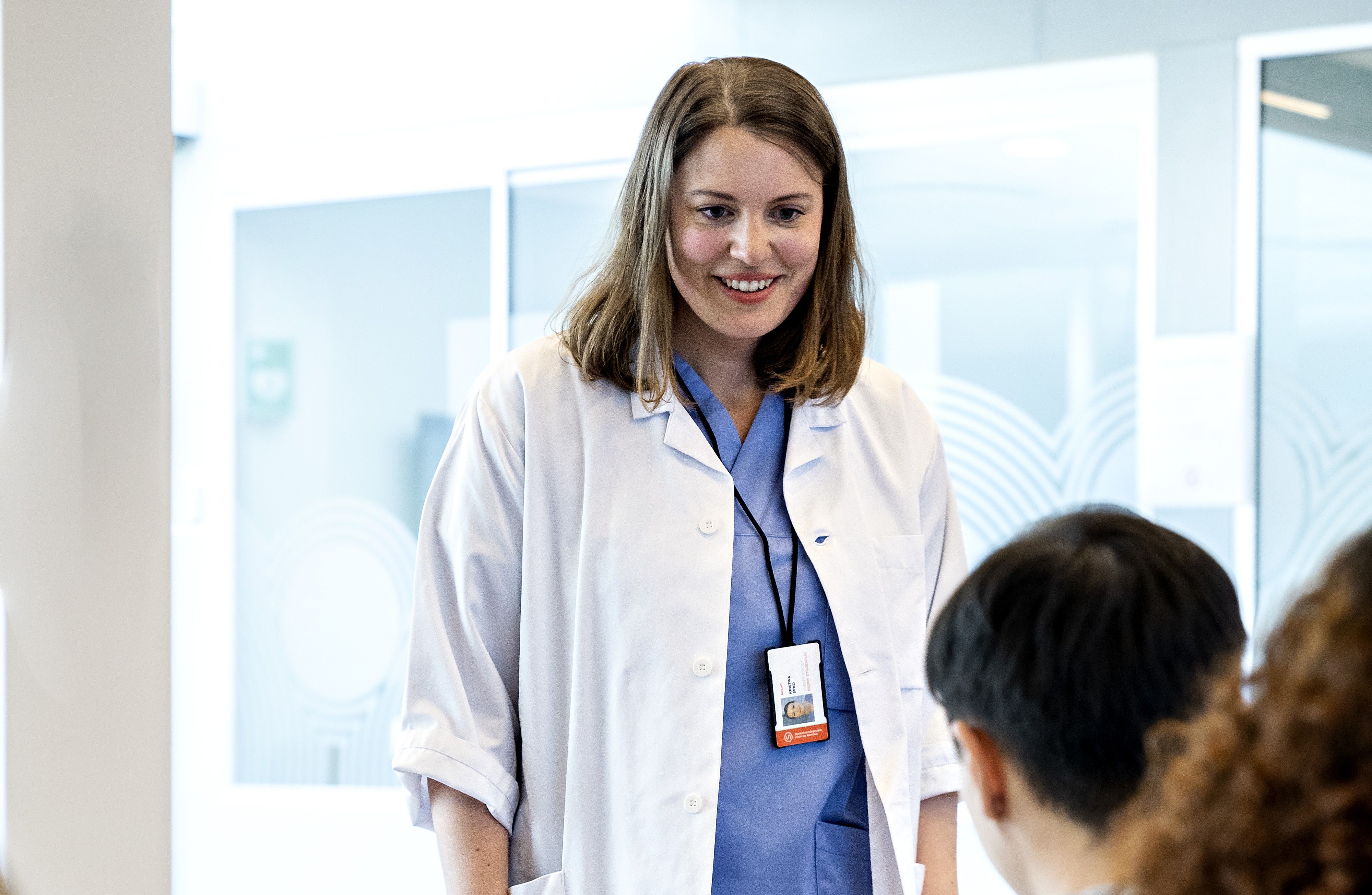 Bilde av en kvinne i legefrakk som smiler til en pasient. Fastlege i SiO for studenter og ansatte ved læresteder i Oslo og Lillestrøm