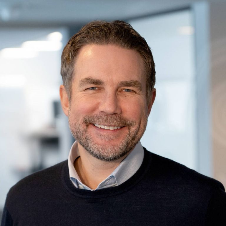 Foto av en mann, Håvard staff Brenno, som smiler med SiO-logo bak seg.