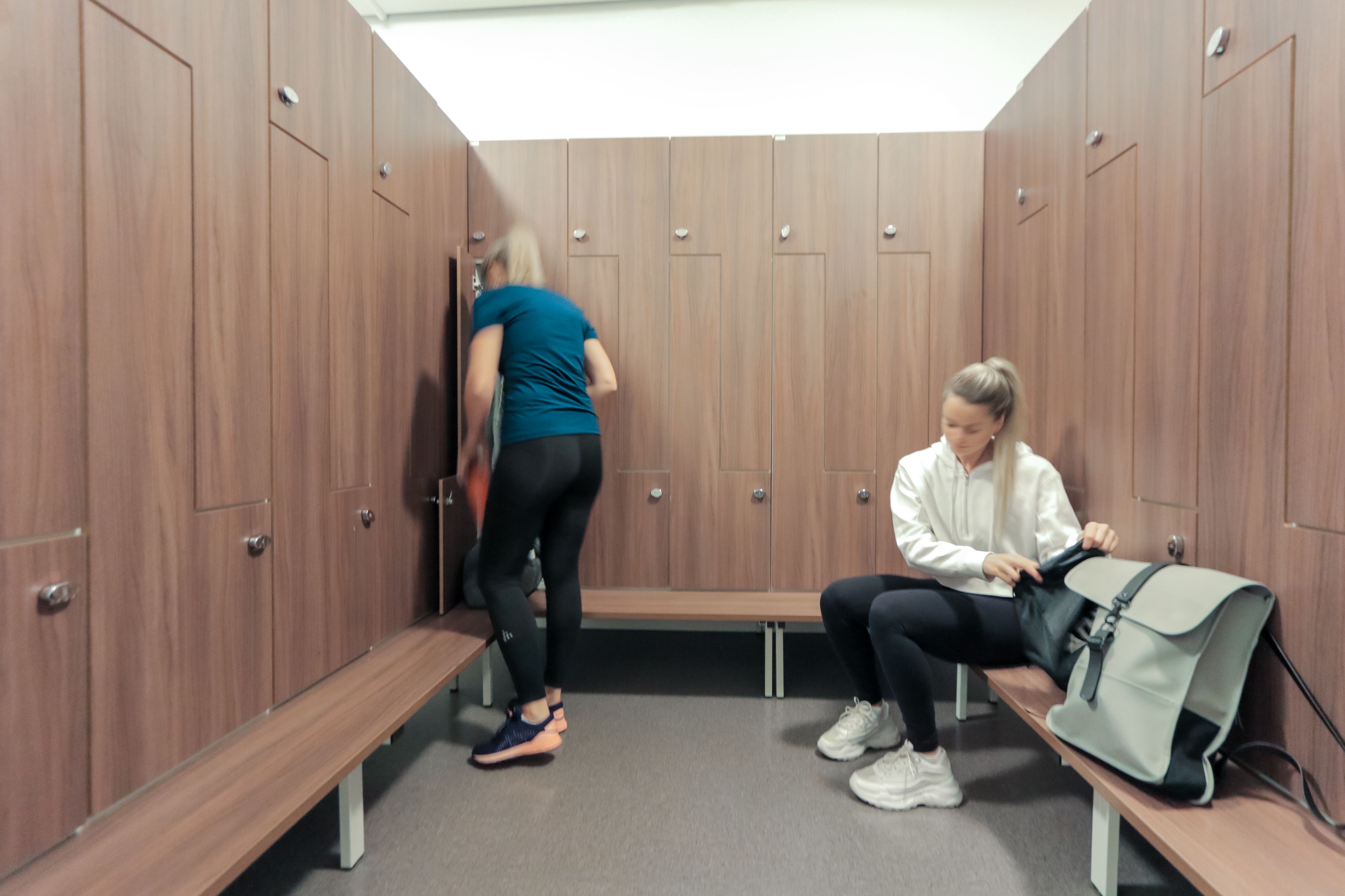 Bilde av deler av damegarderoben på Athletica Blindern med låsbare skap og to personer som pakker sakene sine.