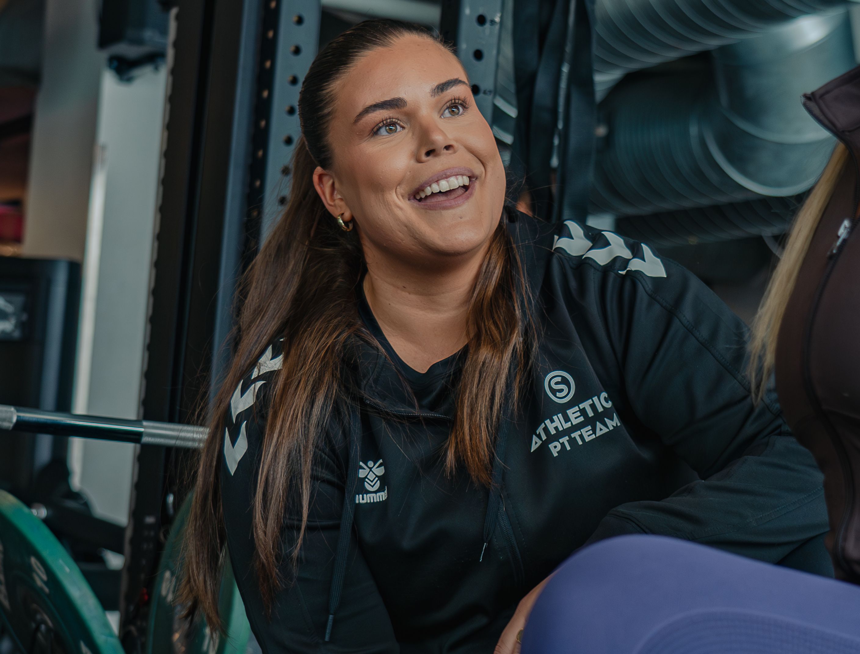 En kvinnelig PT hos SiO Athletica smiler og hjelper en PT kunde.