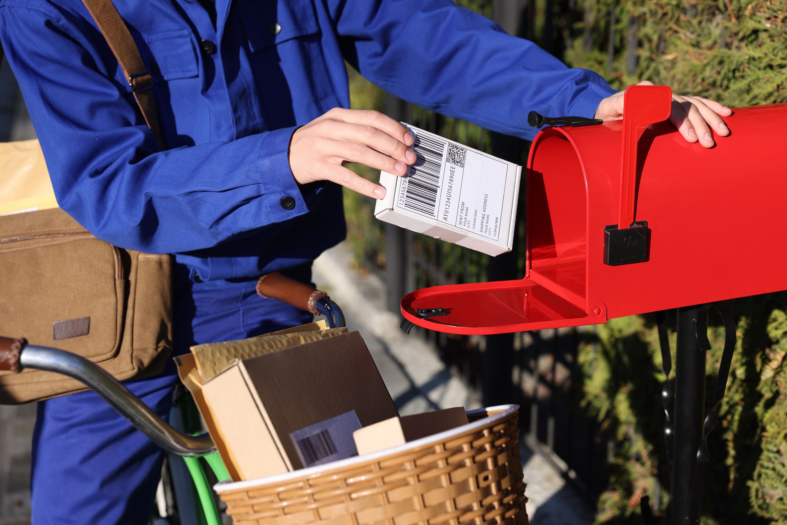 Photo of a person placing a package in a red mailbox.