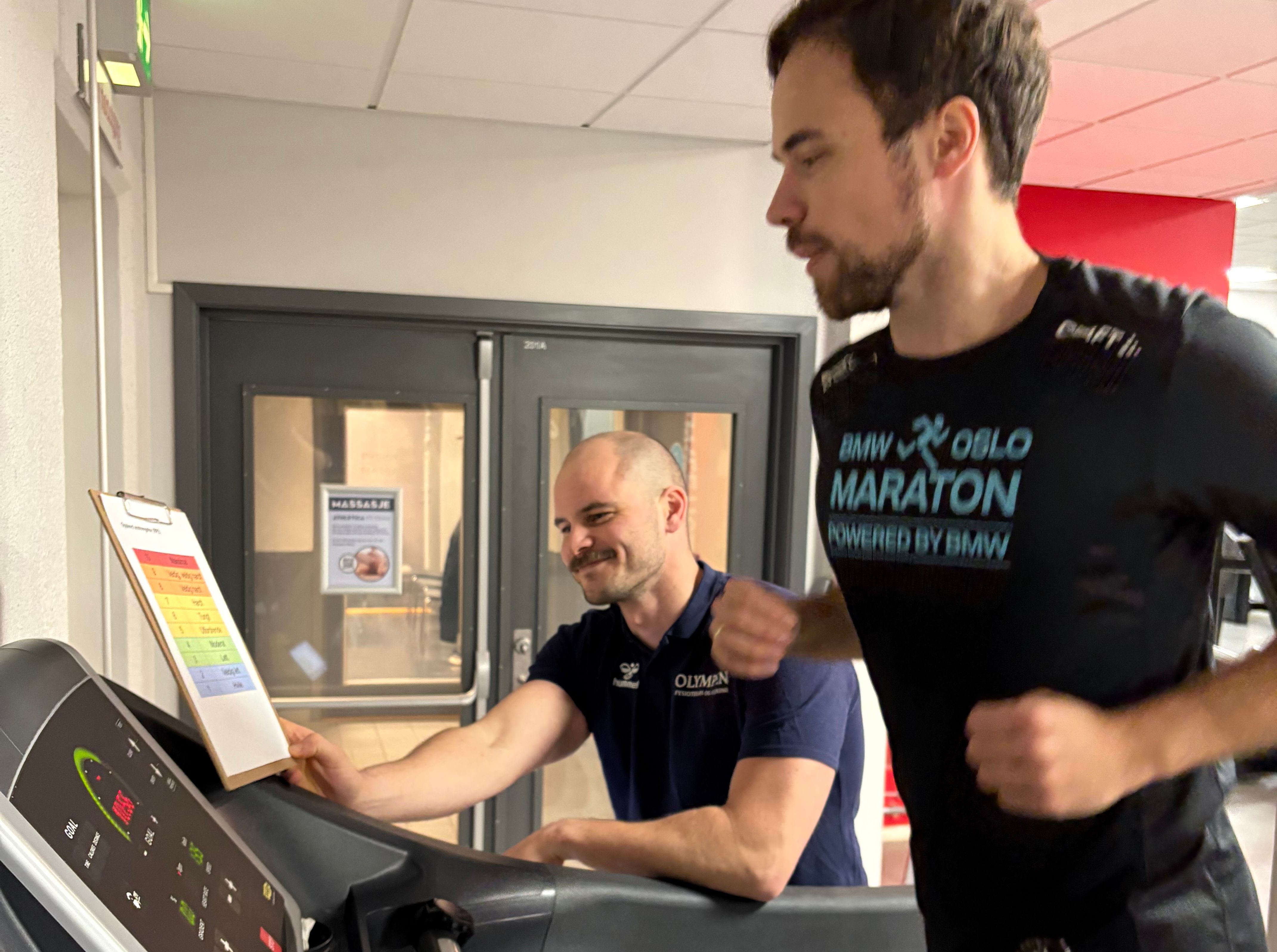 En fysioterapeut følger opp og trener en klient på tredemøllen. 