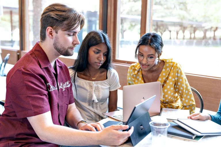 Tre studenter sitter og jobber på datamaskin inne på et spisested.