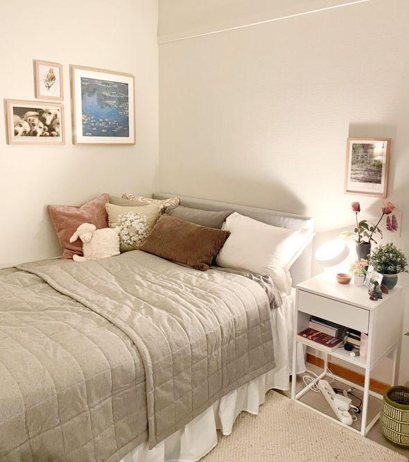 Foto av seng med puter, sengeteppe, nattbord og bilder på veggen. 