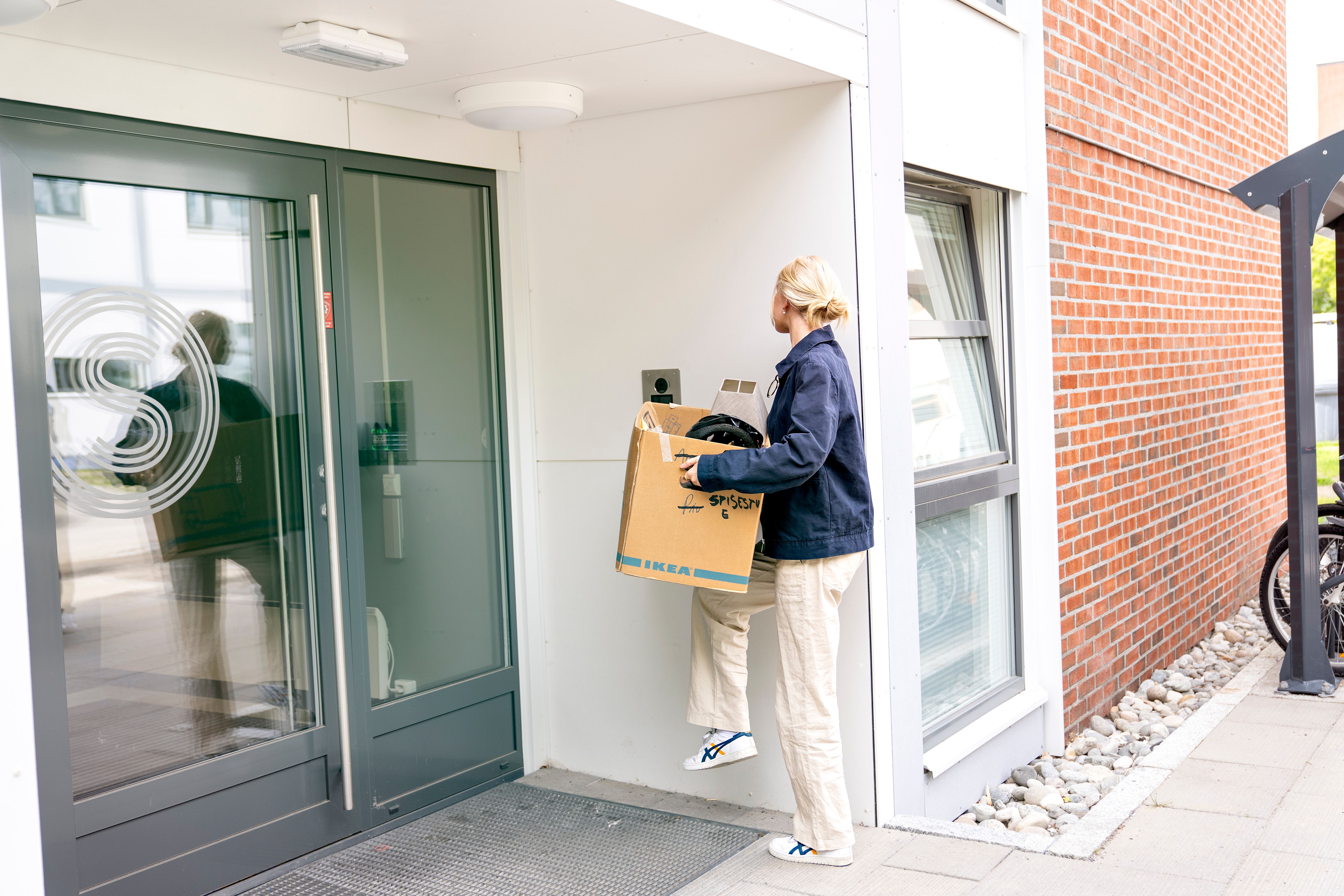 En jente holder en pappeske utenfor en studentbolig, klar for å flytte inn. 
