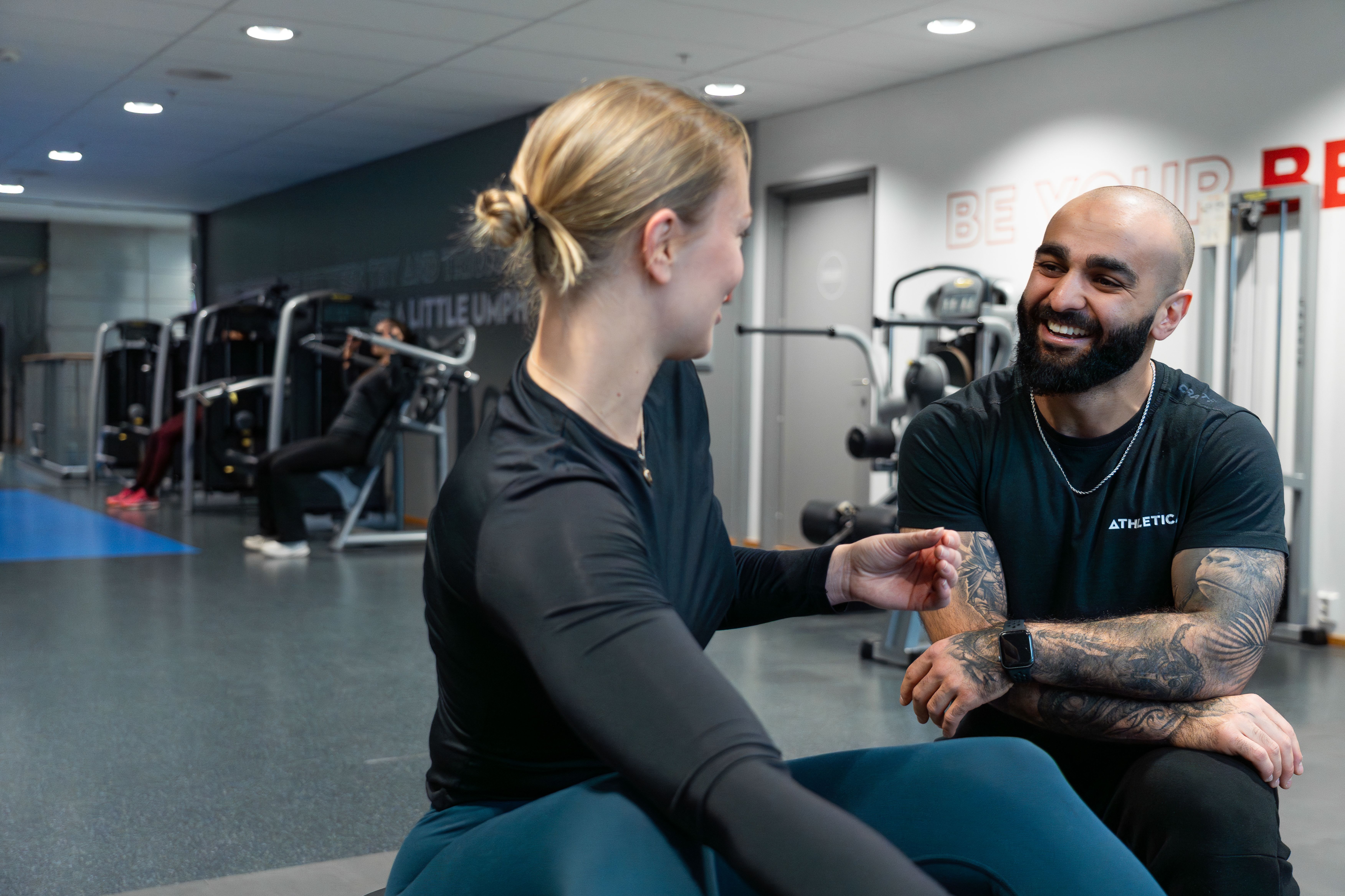 En PT snakker med en PT kunde som trener på et apparat på SiO Athletica Nydalen. 