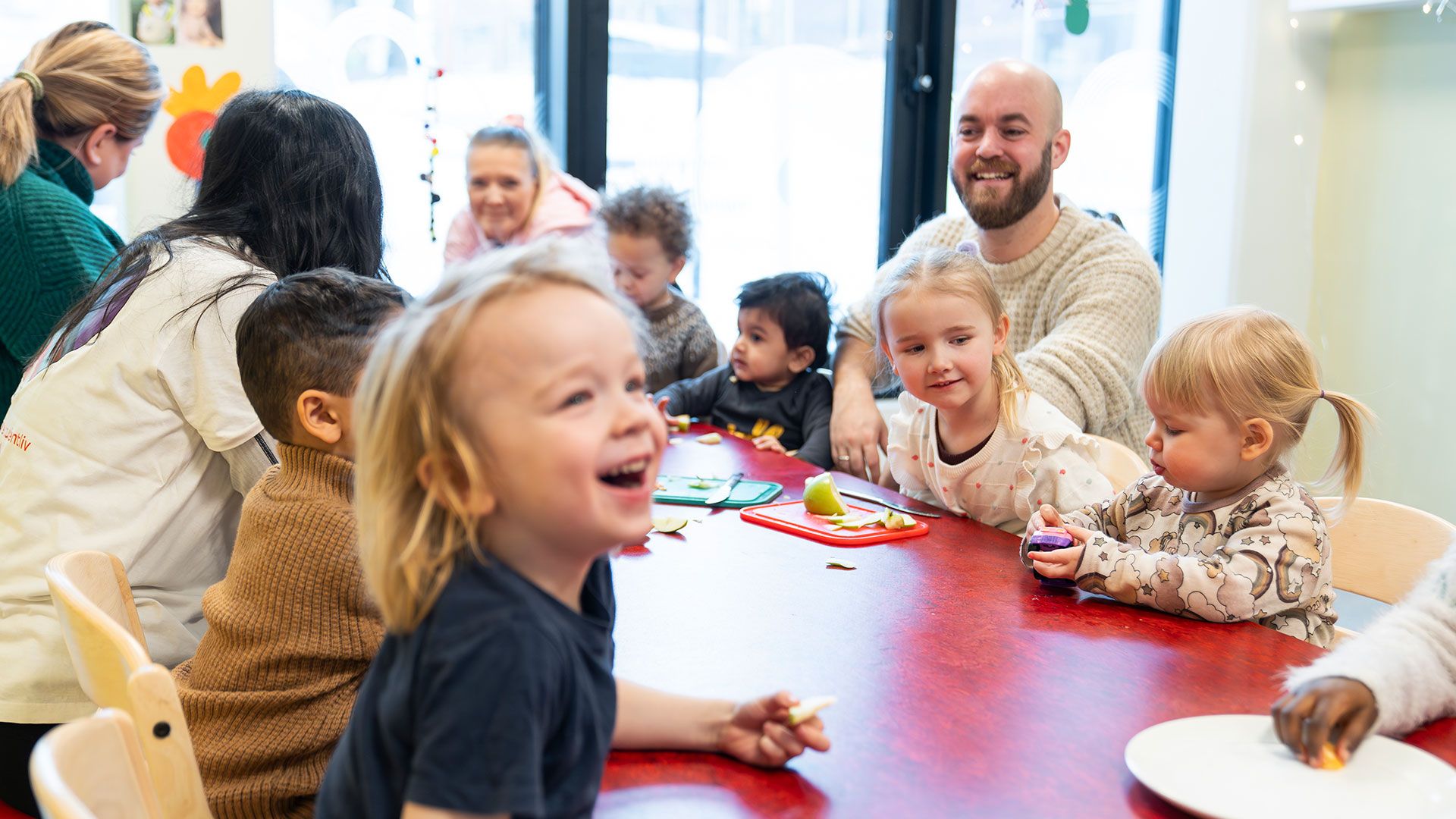 Barn og voksne som sitter rundt et spisebord. De ler og koser seg.