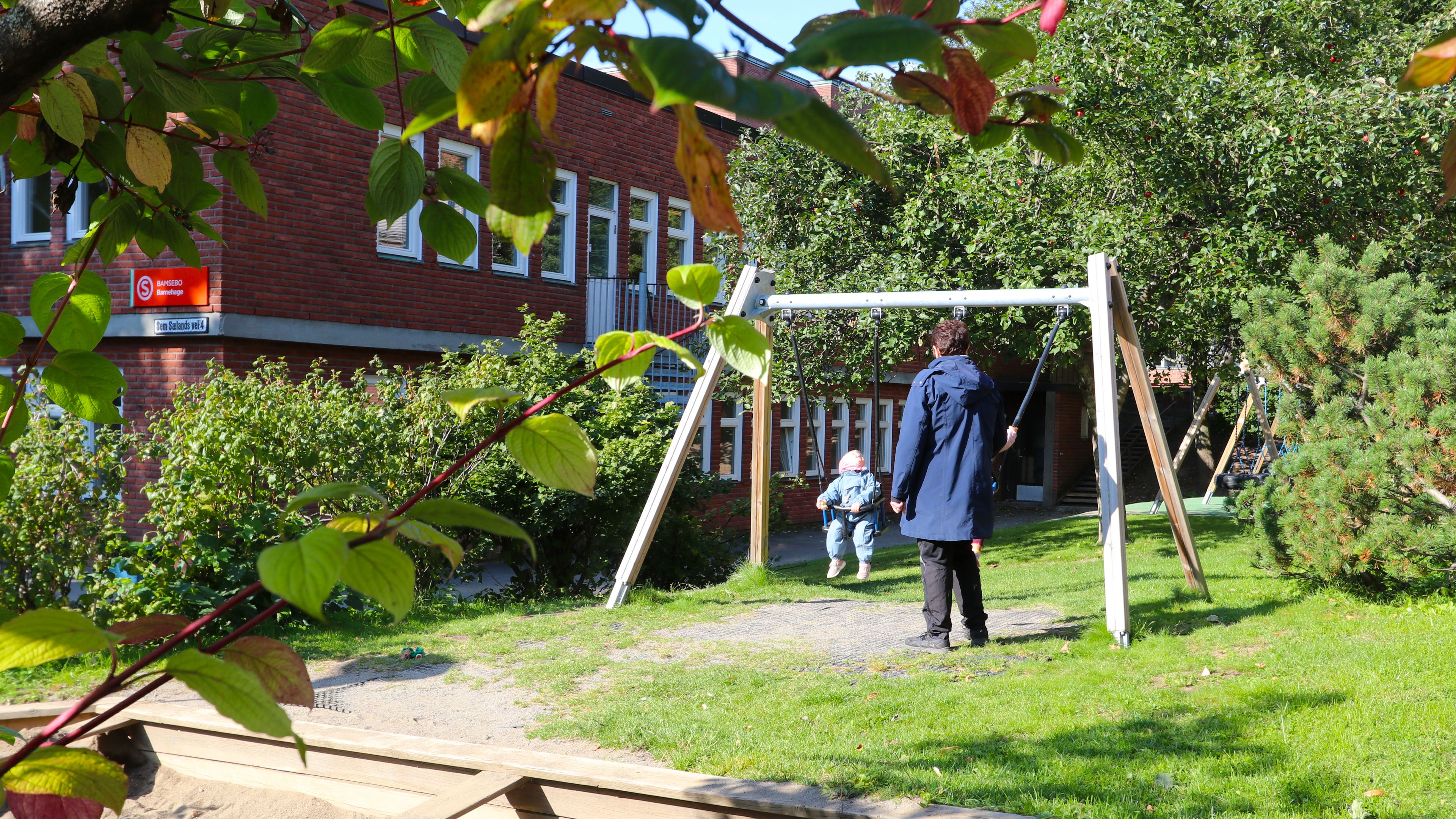 Et barn som sitter på en huske mens en voksen står og passer på