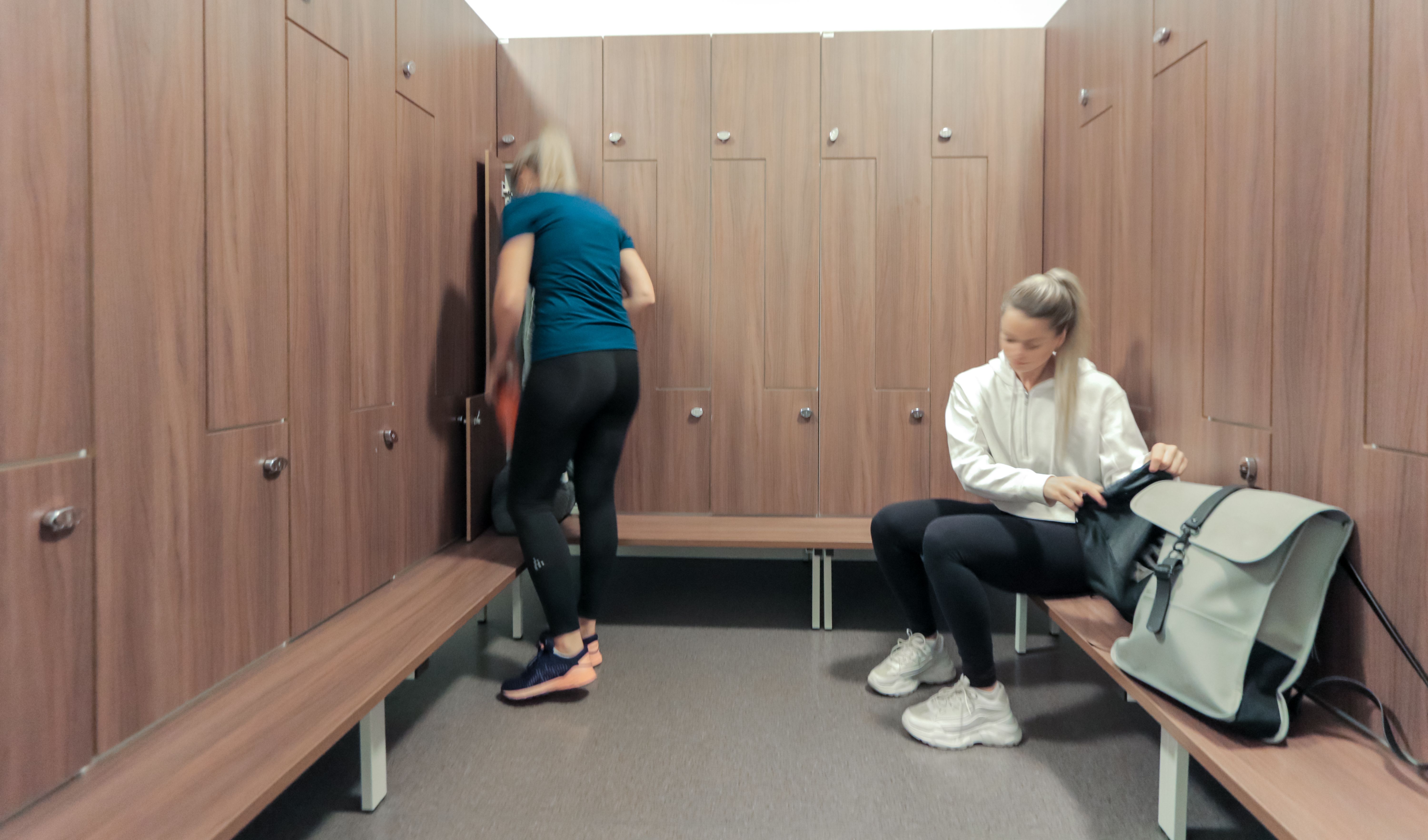 Bilde av deler av damegarderoben på Athletica Blindern med låsbare skap og to personer som pakker sakene sine.