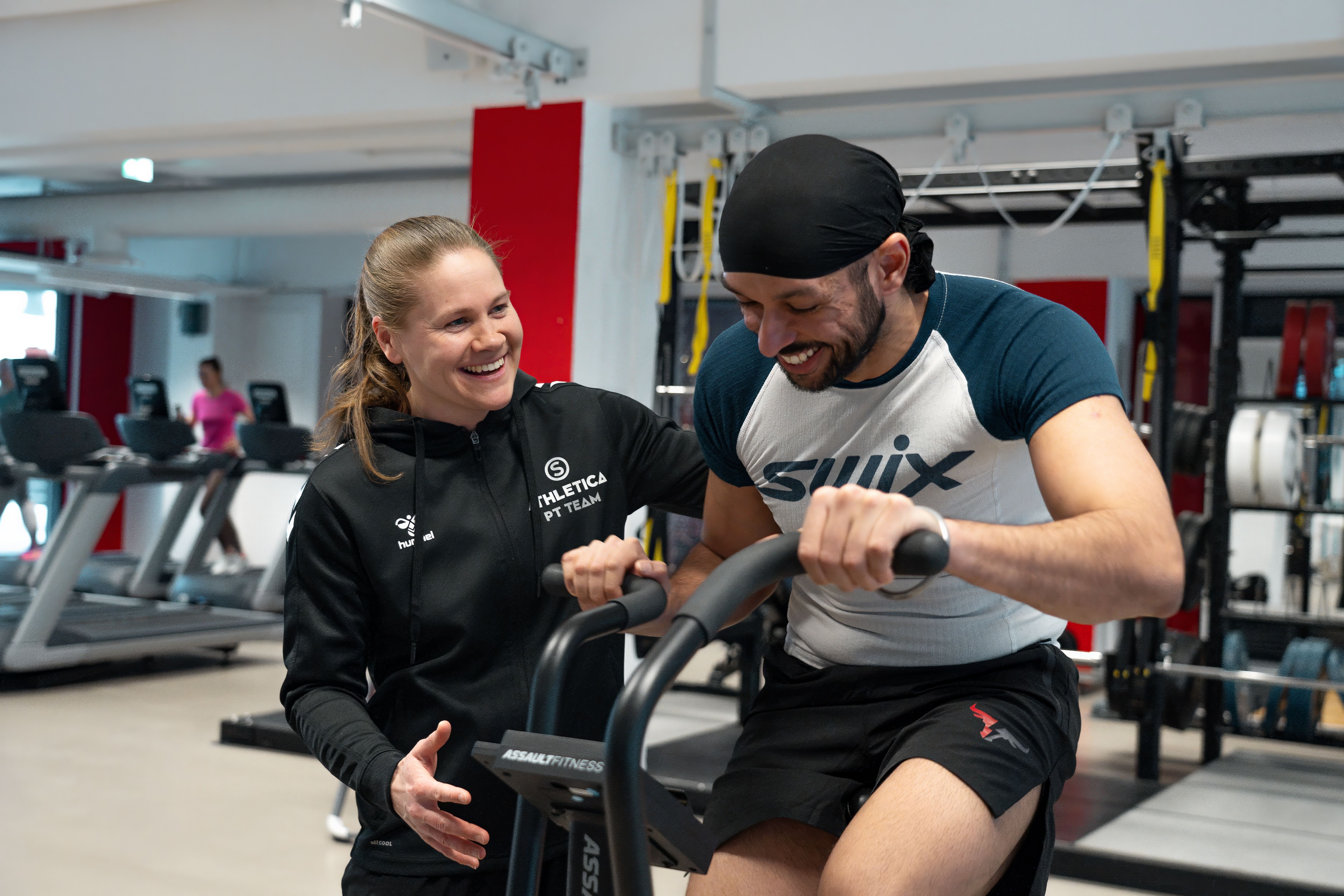En PT som veileder en kunde på assault bike på Athletica Kringsjå. 