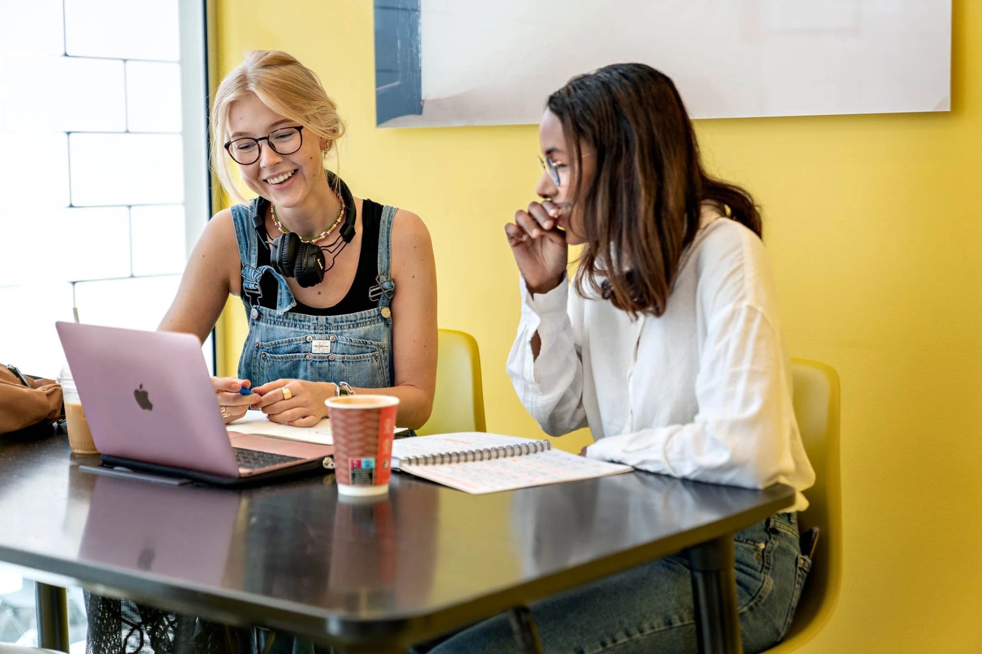 To studenter sitter med datamaskin og skriveblokk og snakker sammen.