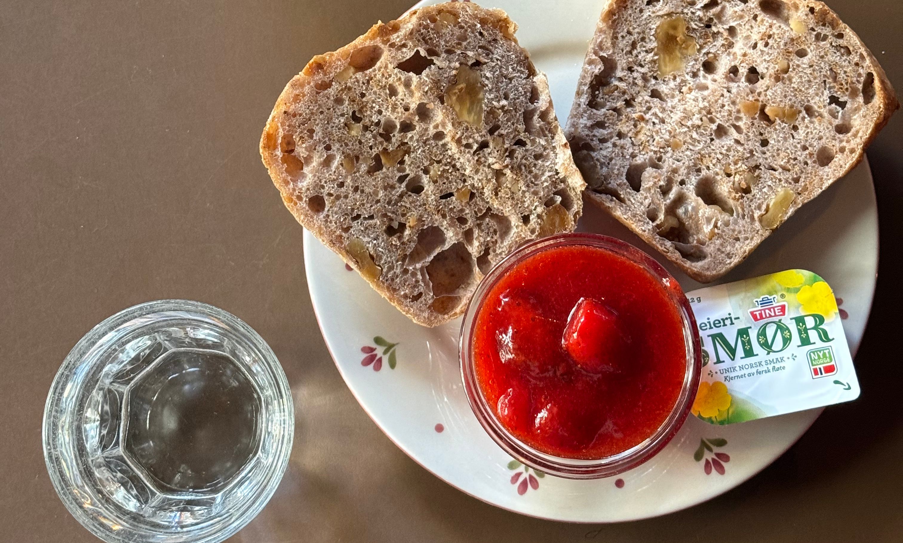 Et innbydende fat med rundstykker, smør og syltetøy med et glass vann