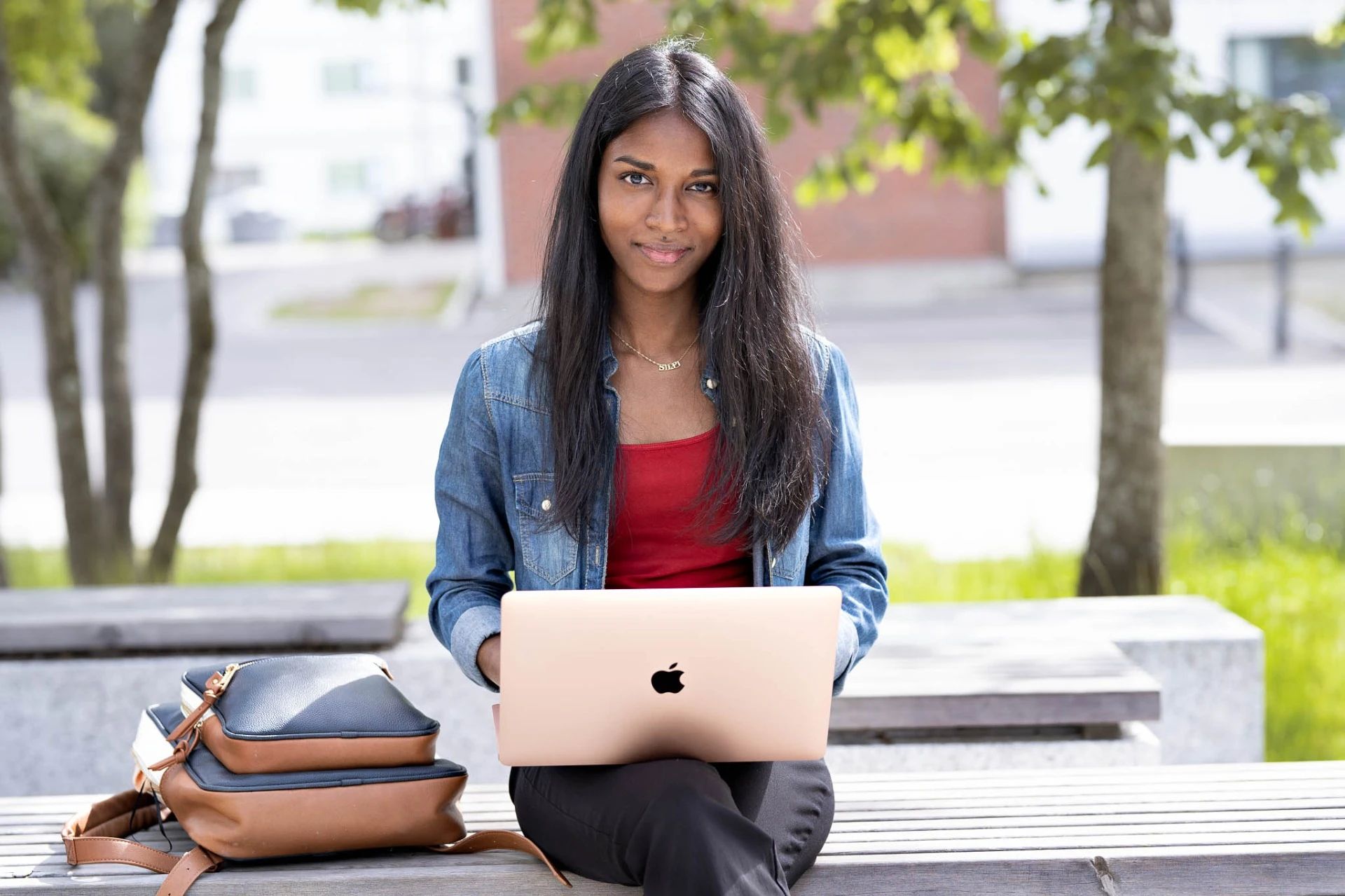 En student som sitter med datamaskin og veske ved siden av seg.