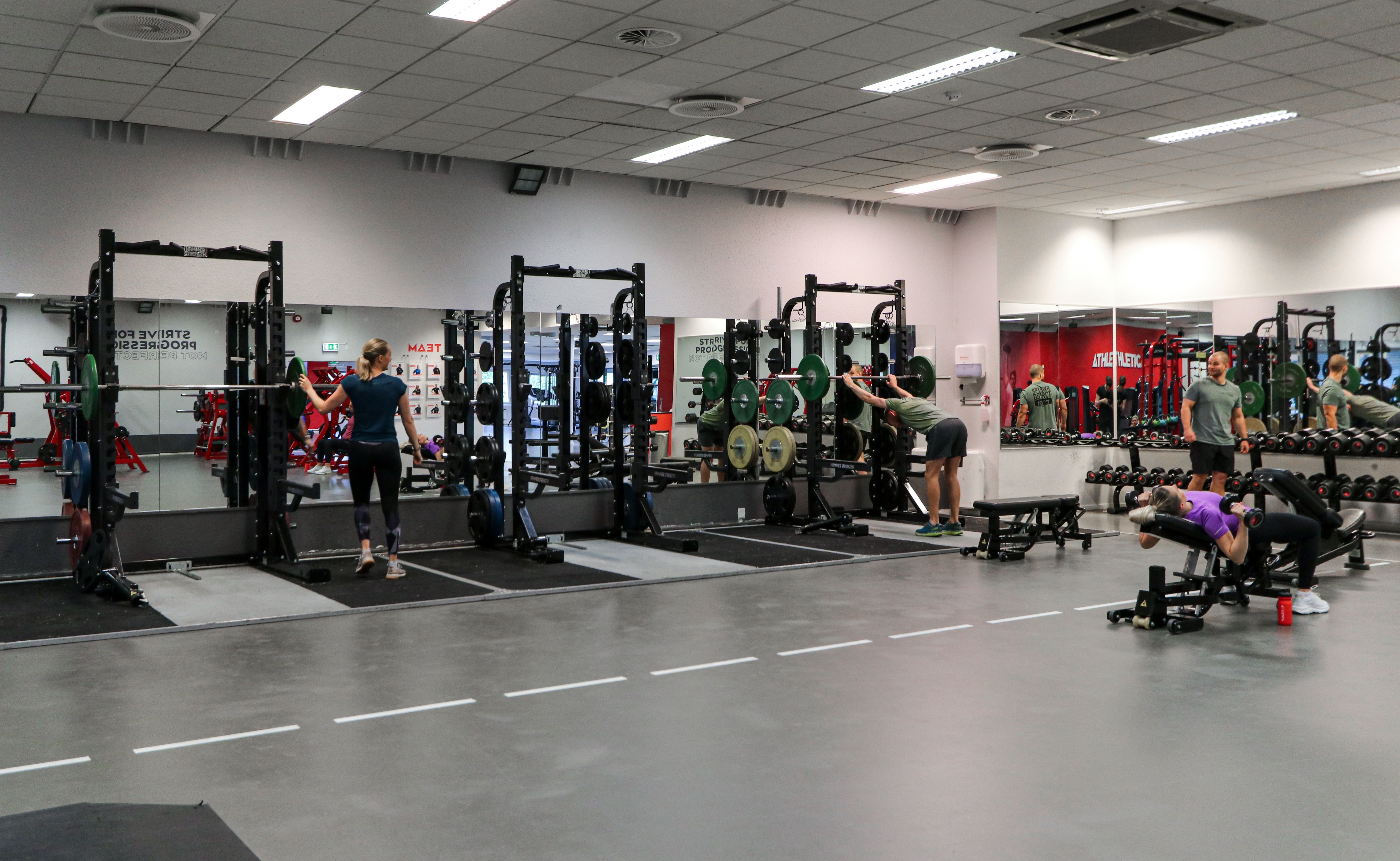 Studio med frivekter og knebøystativ på Athletica Domus og noen som trener. 
