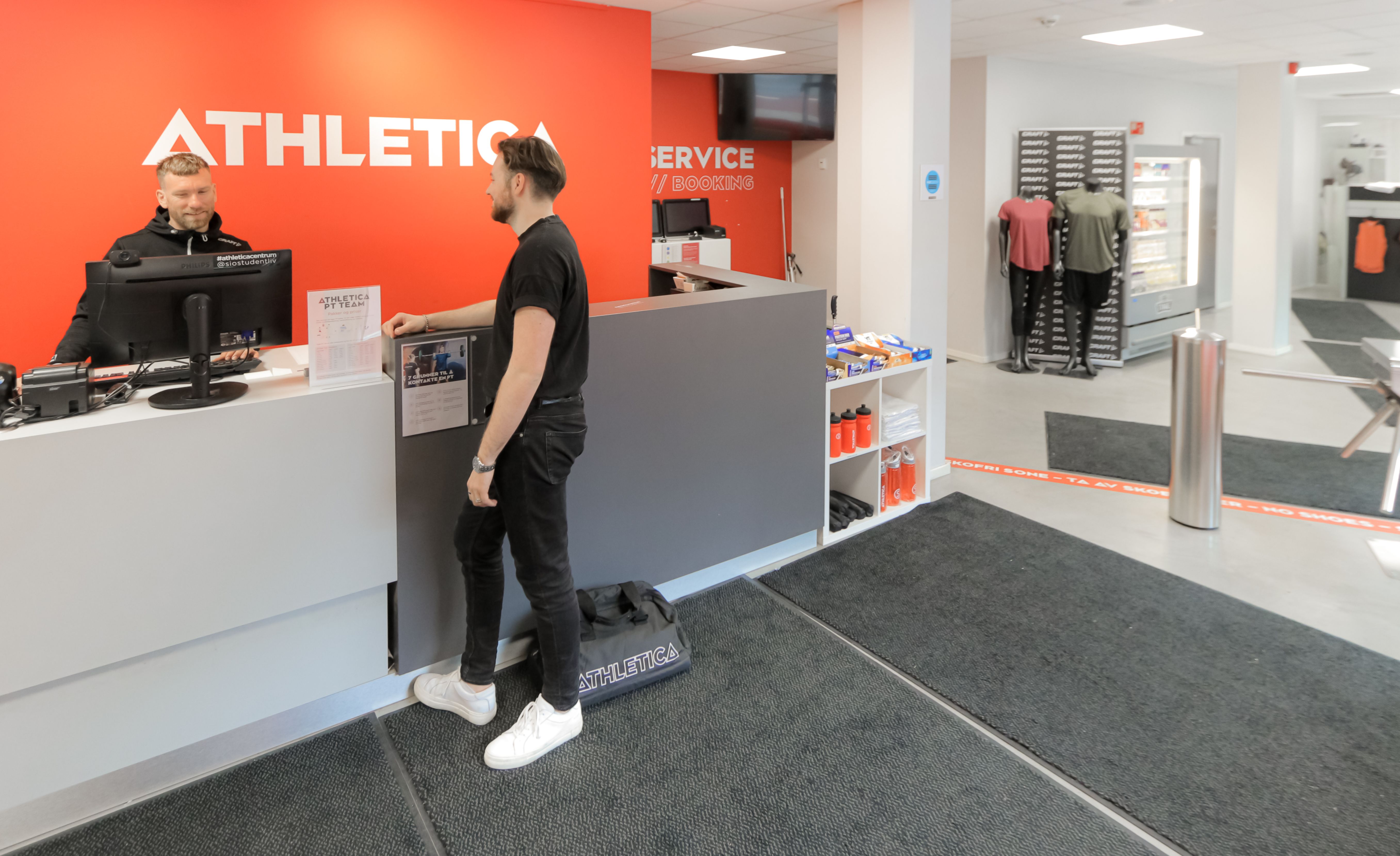 Foto av en mann som får hjelp av en ansatt  i resepsjonen til SiO Athletica Centrum.