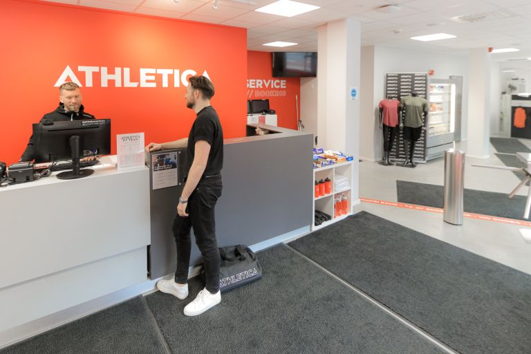 Foto av en mann som får hjelp av en ansatt i resepsjonen til SiO Athletica Centrum.